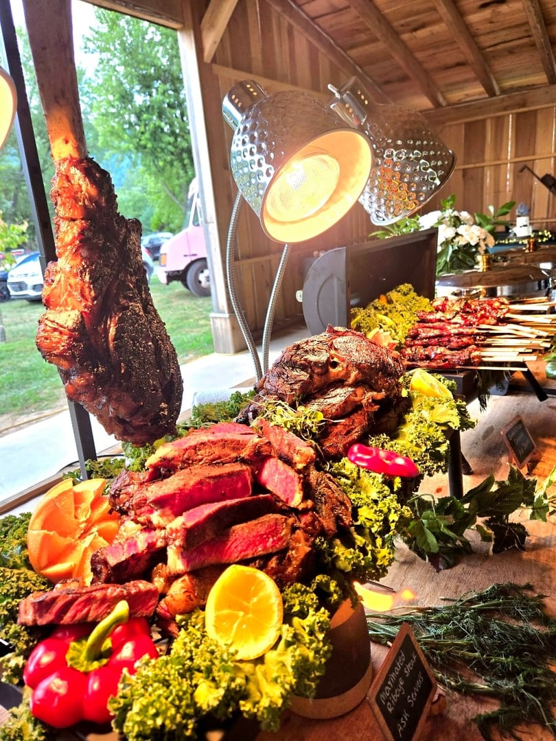 A buffet table laden with carved meats, including a large bone-in roast, sliced steaks, and skewers.